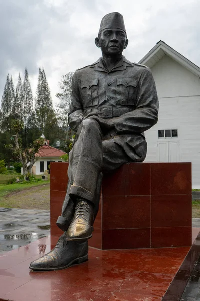 stock image A statue of soekarno, first indonesian president stands by a tree near a memorial monument.