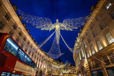 Londra, İngiltere 'de Regent Caddesi boyunca mimarlık. Regent Caddesi 'nin akşam manzarası. Yolun üstünde Noel ışıkları ve kırmızı Londra otobüsü var..