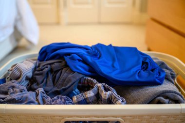 Yatak odasında bir sepet temiz çamaşır. Sepetteki rastgele düzenlenmiş kıyafetler dağınık görünüyor..