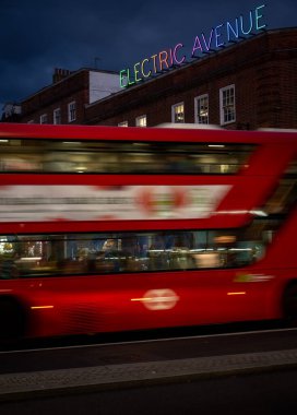 Brixton, Londra, İngiltere: Brixton Yolu boyunca gece boyunca hareket bulanıklığı olan kırmızı bir Londra otobüsü. Elektrik Bulvarı ve renkli neon ışıklarıyla kavşakta..