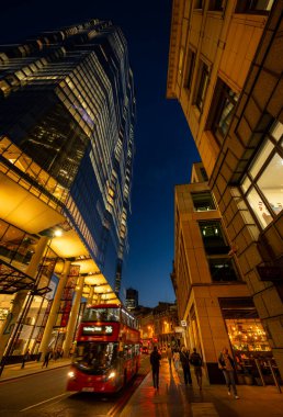 Londra, İngiltere: Kırmızı Londra otobüsü akşam karanlığında Bishopsgate 'de hareket bulanıklığı çekiyor. İnsanlar kaldırım boyunca yürür. 22 Bishopsgate gökdeleni sola.