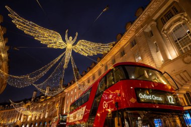 Londra, İngiltere - 20 Kasım 2023: Londra şehir merkezindeki Regent Caddesi 'nde kırmızı Londra otobüsleri ve Noel ışıkları var. Şenlikli meleklere ve aydınlatılmış binalara bakıyorum..