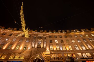 Londra, İngiltere - 20 Kasım 2023: Londra 'nın merkezindeki Regent Caddesi' nde Noel ışıkları tepemizde. Neşeli bir meleğe ve aydınlatılmış binalara bakıyorum..