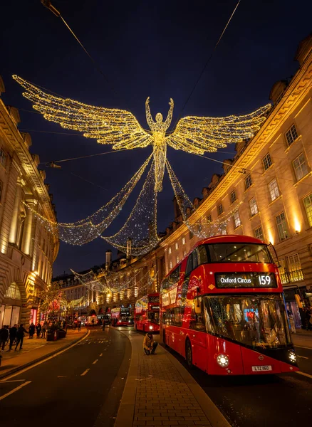 Londra, İngiltere - 20 Kasım 2023: Londra 'nın merkezindeki Regent Caddesi' nde Noel ışıkları tepemizde. İnsanlar Noel alışverişi yapıyor ve üç kırmızı Londra otobüsü yaklaşıyor..