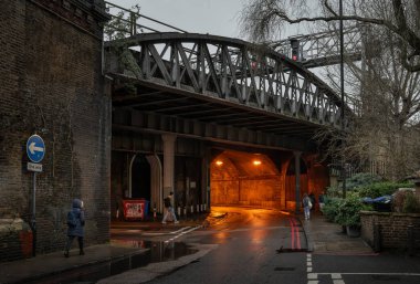 Bermondsey, London, UK: Crucifix Lane passing through a road tunnel under the London Bridge to Greenwich Railway Viaduct in the London borough of Southwark with people walking. clipart