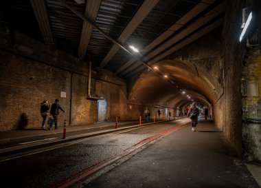 Southwark, London, UK: Bermondsey Street passing through a road tunnel under the London Bridge to Greenwich Railway Viaduct with pedestrians. clipart