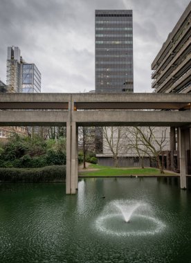 Londra, İngiltere: Londra 'daki Barbican Malikanesi' nde yapay bir gölden geçen yüksek seviyeli bir yürüyüş yolu. Barbican Malikanesi, Londra 'daki Brutalist mimarinin önemli bir örneğidir..