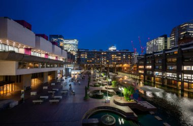Londra, İngiltere: Londra 'daki Barbican Malikanesi' nin gölü ve çeşmeleri olan gece manzarası. Barbican Malikanesi, Londra 'daki Brutalist mimarinin önemli bir örneğidir..