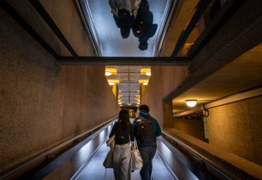 Londra, İngiltere: Londra 'daki Barbican Malikanesi' nin iç mimarisi ve rampada iki kişi var. Barbican Malikanesi, Londra 'daki Brutalist mimarinin önemli bir örneğidir..