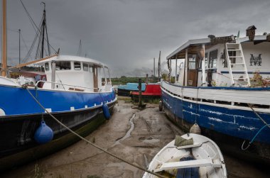 Fırtınalı bir gökyüzünün altında çamurda oturan tekneler. Suffolk, İngiltere 'nin tarihi Woodbridge kasabasındaki Deben Nehri' nin akıntısı altında rıhtımın manzarası..