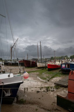 Woodbridge, Suffolk, UK: Fırtınalı bir gökyüzünün altında çamurda oturan tekneler. Woodbridge 'in tarihi kasabasındaki Deben Nehri' nin alçak sularındaki rıhtımın manzarası..