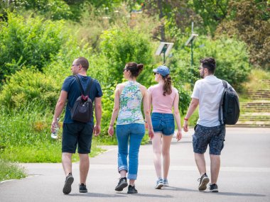 Bükreş, Romanya - Haziran 2022: Güneşli bir yaz gününde parkta gezinen iki genç çiftin arka manzarası.
