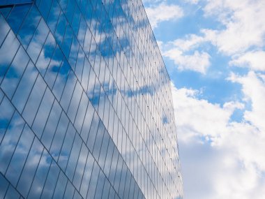 The sky with white clouds reflecting in the glass windows of a modern office building.