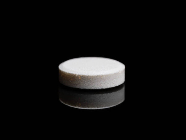 A single isolated pill or medicine tablet on black background
