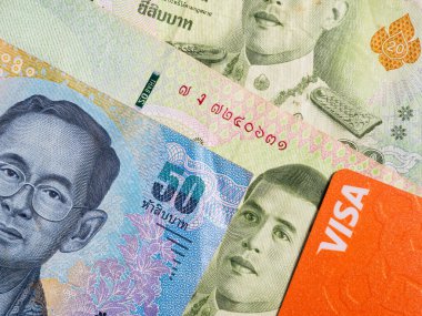 Macro detail with a 50 Thai Baht banknote and a visa debit or credit card. the baht is the official currency of Thailand