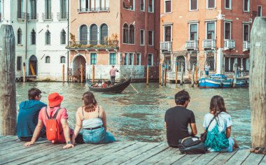 Venedik, İtalya - 30 Mayıs 2023: Tahta bir tekne iskelesinde oturan turistler Venedik 'teki Büyük Kanal' ın cennet manzarasının tadını çıkarıyorlar.