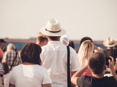 Arkadaki fotoğrafta zarif bir şapka takan bir adam kalabalıkla çevrili..