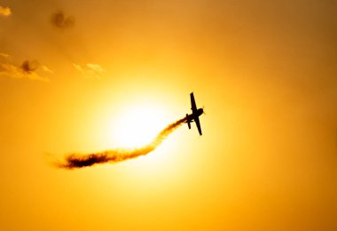 Gün batımında kızıl gökyüzüne doğru uçan akrobatik bir uçağın silüeti..