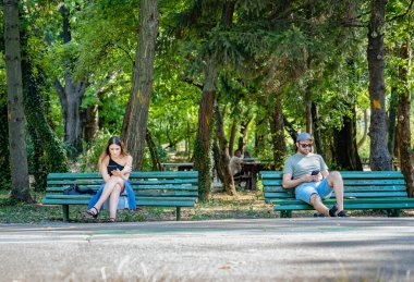 Bükreş, Romanya - 17 Haziran 2023: Kral Mihai I parkında banklarda oturan iki genç.