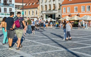 Brasov, Romanya - Eylül 02.2023: Brasov 'un eski şehir merkezindeki yaya bölgesinde turistler ve yerel halk geziniyor. Council Square 'deki belediye binası..