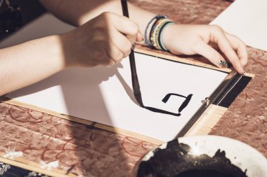 Bir el fırça tutarak ve Asyalı kaligrafisi yazarak kapat