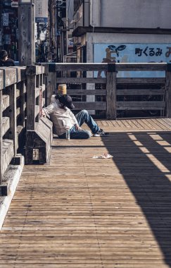 Osaka, Japan, 05.05.2024: Homeless man sleeping on a wooden bridge over Dotonbori river. clipart