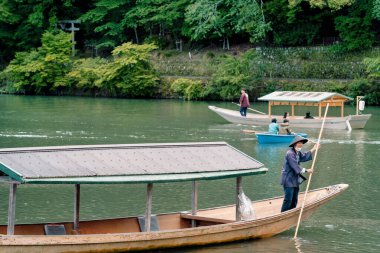 Kyoto, Japonya - 05.07.2024: Arashiyama Katsura nehri üzerinde geleneksel Japon tekne gezisi. Kayıkçı, bambu sopasını kürek olarak kullanıyor..