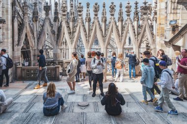 Milan, İtalya - 05.14.2024: Turistler, karmaşık gotik kuleler ve heykellerle çevrili ikonik Duomo di Milano 'nun çatı teraslarında güneşli bir günün tadını çıkarıyorlar.