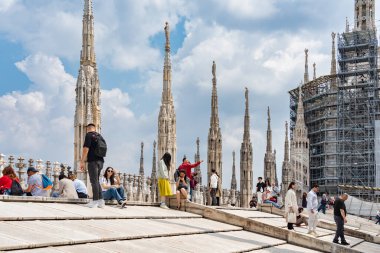 Milan, İtalya - 05.14.2024: Turistler, karmaşık gotik kuleler ve heykellerle çevrili ikonik Duomo di Milano 'nun çatı teraslarında güneşli bir günün tadını çıkarıyorlar.