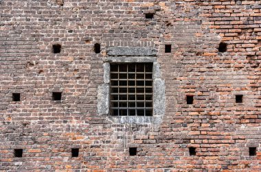 İtalya 'nın Milano kentindeki tarihi Sforza Şatosu' nun (Castello Sforzesco) ağır demir ızgarası tarafından korunan ortaçağ tuğla duvarındaki bir pencerenin yakın çekim görüntüsü,