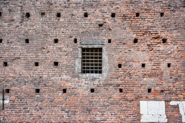 İtalya 'nın Milano kentindeki tarihi Sforza Şatosu' nun (Castello Sforzesco) ağır demir ızgarası tarafından korunan ortaçağ tuğla duvarındaki bir pencerenin yakın çekim görüntüsü,