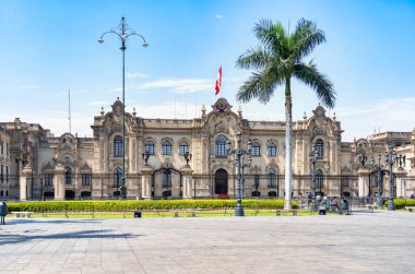 Lima, Peru - 11 Mart 2025: Güneşli bir günde arka planda, Peru Hükümet Sarayı (Palacio de Gobierno) ile Plaza Belediye Başkanı boyunca yürüyen turistler.