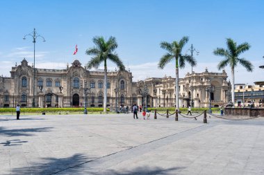 Lima, Peru - 11 Mart 2025: Güneşli bir günde arka planda, Peru Hükümet Sarayı (Palacio de Gobierno) ile Plaza Belediye Başkanı boyunca yürüyen turistler.