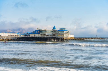 Arkasında Pasifik Okyanusu ve Chorrillos tepeleri olan Miraflores rıhtımında bir restoran manzarası.