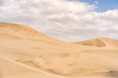 Golden sand dunes of Ica desert under a clear blue sky in Huacachina, Peru