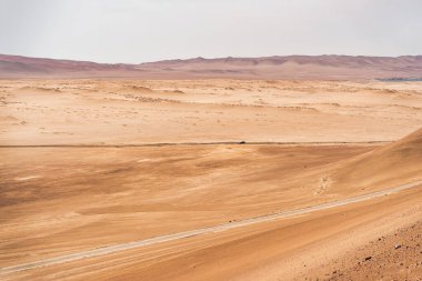 Peru 'daki Paracas Ulusal Rezervi' nin engin çöl manzarasından geçen bir araba..