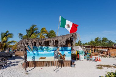 Holbox Mexico 12 04 2023: Mavi gökyüzü üzerinde küçük kulübesi, çiftliği ve palmiye ağaçları olan Meksika bayrağı.