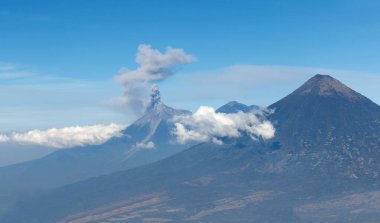Guatemala 'da ufukta dağ sırasına karşı kümülüs bulutları arasında yükselen dumanlı bir kalkan volkanı vardır..