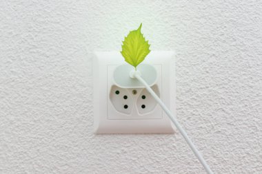 Elektrik prizindeki telefon şarj aleti veya yeşil enerji ve çevreyi sembolize eden yeşil yapraklı tel prizi..