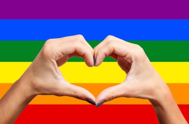 Igbtq gökkuşağı renkli bayrağından elleri olan bir kadın kalp şekli yaratıyor.