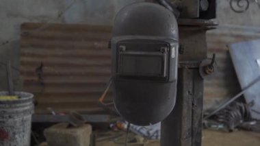 Görüntü bir demirci dükkanına yerleştirilmiş, kullanılmaya hazır bir kaynak başlığı gösteriyor. Kask, kaynakçıların güvenliğini sağlamak için gerekli koruyucu ekipman.