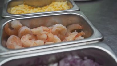 Görüntü, gurme pizzası için taze karides seçimi ile aşçılık hazırlıklarını gösteriyor. Uzman eller her karidesi dikkatlice seçerek, içeriğinin detaylarına ve kalitesine dikkat çeker.