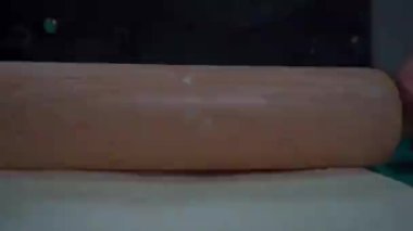 Detaylı çekim pizza hamurunu germek için kullanılan merdaneye odaklanıyor. Sahne, zanaat pizzası hazırlamada en önemli aracı vurguluyor