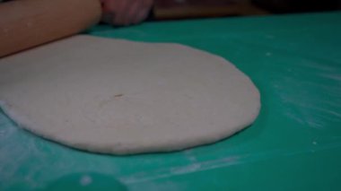Pizza hamurunu germek için kullanılan tahta raptiye. Sahne sanatsal pizza hazırlığının bu kilit adımındaki hassasiyet ve özeni yakalıyor.