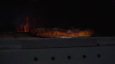 Pizzanın mükemmel şekline ulaştığı anı yakalar, geleneksel ahşap fırının ısısının pizzaya son dokunuşu nasıl yaptığını gösterir, dokusunu ve tadını arttırır..