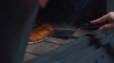 Fırındaki pizza hamurunu kontrol ederken yemek pişirmenin en önemli anını yakalıyor. Görüntü hamurun dokusunun ve kahverengisinin nasıl değerlendirildiğini vurguluyor ve her pizzanın en uygun şekle ulaşmasını sağlıyor.