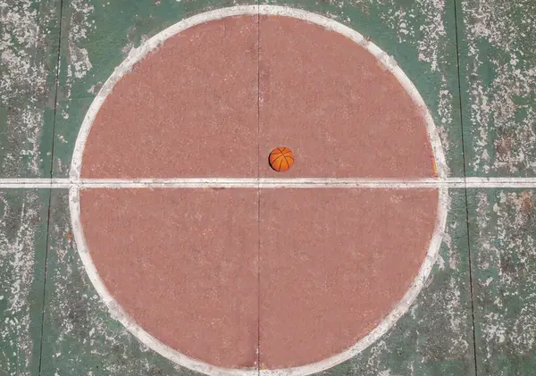 Topun merkezde yer aldığı bir basketbol sahasının yukarıdan görünüşü, alanın tasarım ve düzenini yakalıyor. Bu perspektif alan ve top arasındaki karşıtlığı vurgular