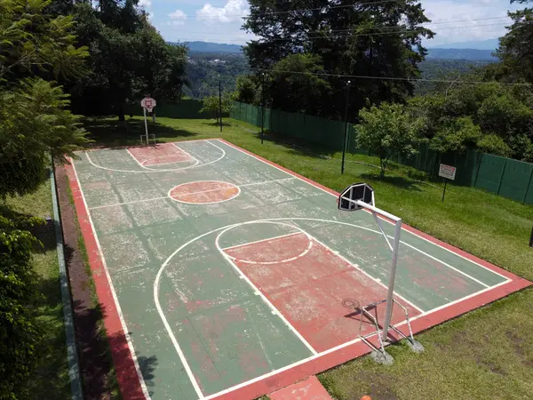 Kırsal bir açık hava basketbol sahasının panoramik görüntüsü, sadeliği ve otantik karakteri gösteriyor..