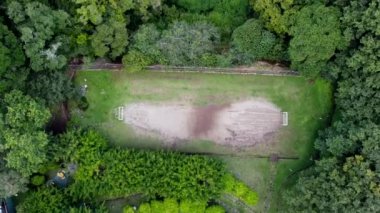 Futbol sahasının yukarıdan görünüşü, doğal bir ortamın ortasında yer alıyor. Yukarıdaki perspektif bitki örtüsüyle çevrili alanı gösteriyor, oyun alanının çevresindeki doğal manzarayla uyum içinde nasıl bütünleştiğini vurguluyor