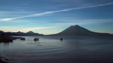 Görkemli Atitlan Gölü tamamen temiz bir gökyüzünün altında. Gölün suları gökyüzünün maviliğini yansıtırken, etrafındaki volkanlar ve dağlar tüm ihtişamıyla gösterilir.